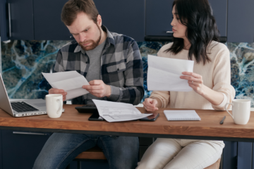 Older Plano homeowner reviewing property tax statements and a home-sale planning worksheet with an advisor at a bright kitchen table